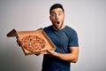 Young handsome man holding delivery box with delicious Italian pizza over white background scared in shock with a surprise face, Royalty Free Stock Photo