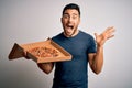 Young handsome man holding delivery box with delicious Italian pizza over white background very happy and excited, winner Royalty Free Stock Photo