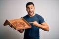 Young handsome man holding delivery box with delicious Italian pizza over white background very happy pointing with hand and Royalty Free Stock Photo