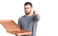 Young handsome man holding delivery italian pizza pointing with finger to the camera and to you, confident gesture looking serious Royalty Free Stock Photo