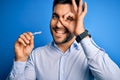 Young handsome man holding dental aligner tooth correction over blue background with happy face smiling doing ok sign with hand on Royalty Free Stock Photo