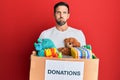 Young handsome man holding donation box with toys puffing cheeks with funny face