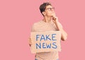 Young handsome man holding fake news banner serious face thinking about question with hand on chin, thoughtful about confusing