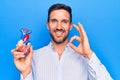 Young handsome man holding heart organ with veins and arteries over blule background doing ok sign with fingers, smiling friendly