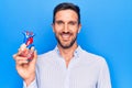 Young handsome man holding heart organ with veins and arteries over blule background looking positive and happy standing and