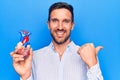 Young handsome man holding heart organ with veins and arteries over blule background pointing thumb up to the side smiling happy Royalty Free Stock Photo