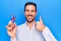 Young handsome man holding heart organ with veins and arteries over blule background smiling happy and positive, thumb up doing