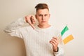 Young handsome man holding Ireland Irish flag over isolated white background with angry face, negative sign showing dislike with Royalty Free Stock Photo