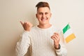 Young handsome man holding Ireland Irish flag over isolated white background pointing and showing with thumb up to the side with Royalty Free Stock Photo