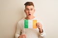 Young handsome man holding Ireland Irish flag over isolated white background scared in shock with a surprise face, afraid and Royalty Free Stock Photo