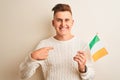 Young handsome man holding Ireland Irish flag over isolated white background with surprise face pointing finger to himself Royalty Free Stock Photo