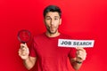 Young handsome man holding magnifying glass for job search making fish face with mouth and squinting eyes, crazy and comical