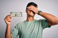 Young handsome man holding one dollar banknotes over isolated white background stressed with hand on head, shocked with shame and Royalty Free Stock Photo