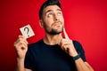 Young handsome man holding paper with question mark symbol over red background serious face thinking about question, very confused Royalty Free Stock Photo