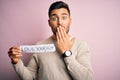 Young handsome man holding paper with self love message over pink background cover mouth with hand shocked with shame for mistake,