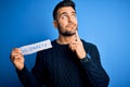 Young handsome man holding paper with solidarity message over blue background serious face thinking about question, very confused Royalty Free Stock Photo