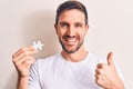 Young handsome man holding piece of puzzle standing over isolated white background smiling happy and positive, thumb up doing Royalty Free Stock Photo