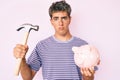 Young handsome man holding piggy bank and hammer depressed and worry for distress, crying angry and afraid Royalty Free Stock Photo