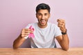 Young handsome man holding pink cancer ribbon screaming proud, celebrating victory and success very excited with raised arms Royalty Free Stock Photo