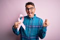 Young handsome man holding pink cancer ribbon symbol over isolated background screaming proud and celebrating victory and success Royalty Free Stock Photo