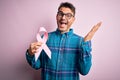 Young handsome man holding pink cancer ribbon symbol over isolated background very happy and excited, winner expression Royalty Free Stock Photo