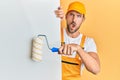 Young handsome man holding roller painter over white banner in shock face, looking skeptical and sarcastic, surprised with open Royalty Free Stock Photo