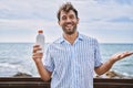 Young handsome man holding sunscreen lotion celebrating achievement with happy smile and winner expression with raised hand Royalty Free Stock Photo