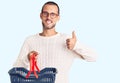 Young handsome man holding supermarket shopping basket smiling happy and positive, thumb up doing excellent and approval sign Royalty Free Stock Photo