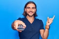 Young handsome man holding television remote control smiling happy pointing with hand and finger to the side Royalty Free Stock Photo