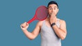 Young handsome man holding tennis racket covering mouth with hand, shocked and afraid for mistake