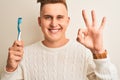 Young handsome man holding tooth brush standing over isolated white background doing ok sign with fingers, excellent symbol Royalty Free Stock Photo