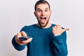 Young handsome man holding tv remote control pointing thumb up to the side smiling happy with open mouth Royalty Free Stock Photo