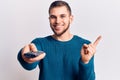 Young handsome man holding tv remote control smiling happy pointing with hand and finger to the side Royalty Free Stock Photo