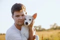 Young handsome man hugging cute white puppy in warm sunset light in summer meadow. Person caressing adorable fluffy puppy.