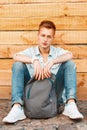 Young handsome man in jeans clothes with a backpack sitting near Royalty Free Stock Photo