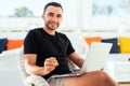 Young handsome man with laptop pointed bitcoin on camera sitting on deck at beack cafe on summer vocation. Man check bitcoin value