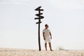 Young handsome man in light clothing and sunglasses near in the desert. column with plates to indicate the direction. Concept of Royalty Free Stock Photo