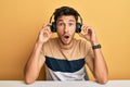 Young handsome man listening to music wearing headphones afraid and shocked with surprise and amazed expression, fear and excited