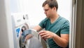 Young handsome man loading dirty clothes in washing machine and doing laundry. Male housework and daily routine at home Royalty Free Stock Photo