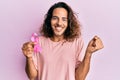 Young handsome man with long hair holding pink cancer ribbon screaming proud, celebrating victory and success very excited with Royalty Free Stock Photo