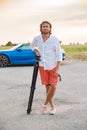 A young handsome man with long hair stands with a tripod somewhere on a country road, the photographer artist arrived in Royalty Free Stock Photo