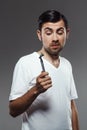 Young handsome man looking at shaver over grey background. Royalty Free Stock Photo