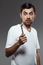 Young handsome man looking at shaver over grey background. Royalty Free Stock Photo