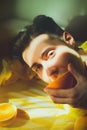 A young, handsome man lying on a yellow bed, savoring a juicy orange half on a sunny summer day. Relaxation, and the simple Royalty Free Stock Photo