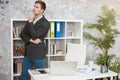 Young handsome man manager standing near his working place in office looking thoughtful at the end of day. multitasking, work Royalty Free Stock Photo