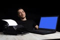 Man midway between a typewriter and laptop on black background in low key.The concept of the past and the future Royalty Free Stock Photo