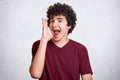 Young handsome man over white background shouts something loud with hands over mouth. Teenager with curly hair and little beard Royalty Free Stock Photo