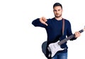 Young handsome man playing electric guitar with angry face, negative sign showing dislike with thumbs down, rejection concept Royalty Free Stock Photo