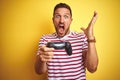 Young handsome man playing video games using joystick game pad over yellow background very happy and excited, winner expression Royalty Free Stock Photo