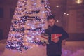 Young handsome man with presents while waiting for someone in the city street with Christmas decorations Royalty Free Stock Photo